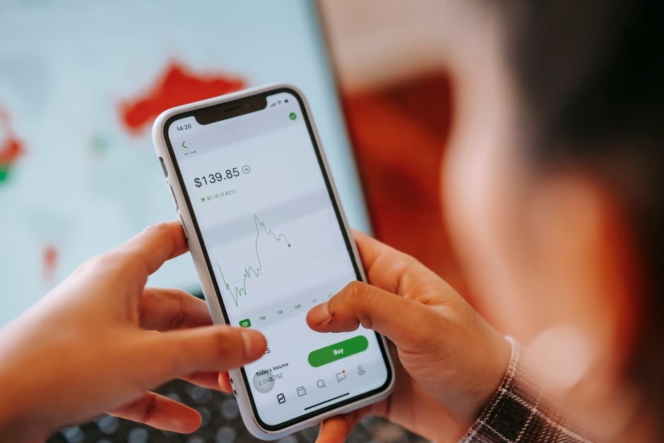 Crop anonymous trader using app on cellphone with graph and dollar price on screen in house