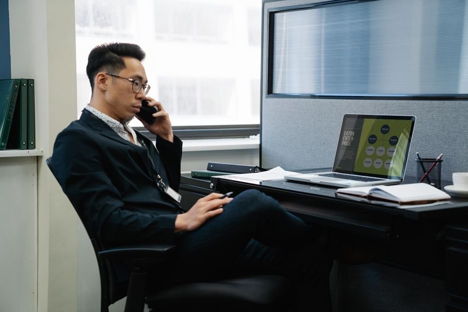 Man in a suit working in an office, talking on phone with laptop and documents.