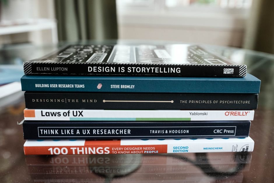 A close-up of books focused on design and UX research stacked on a glass table.
