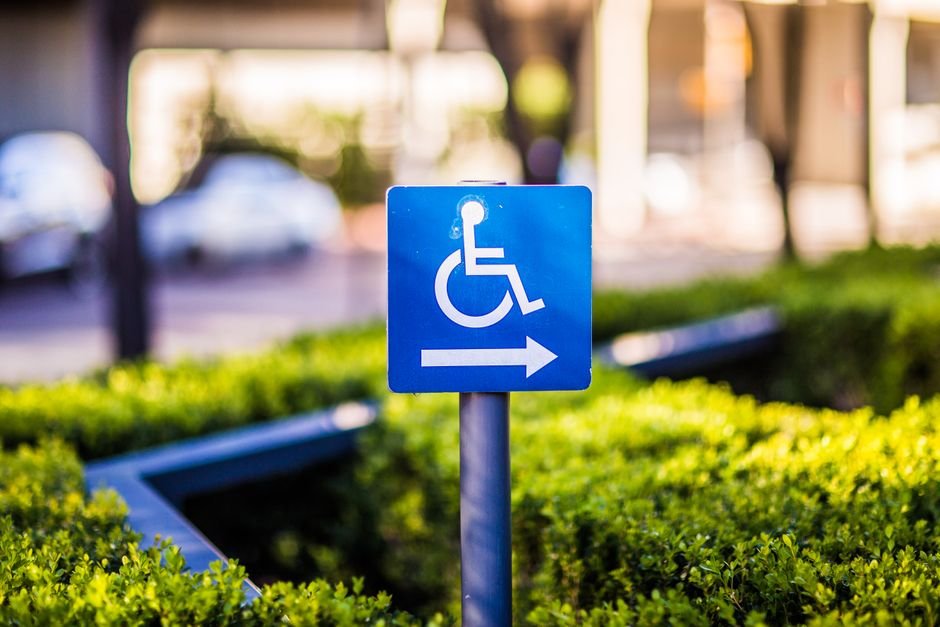 Close-up of a blue directional sign for accessible parking amidst urban greenery.