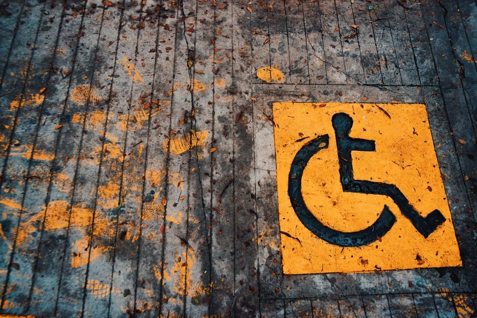Yellow wheelchair accessibility sign painted on urban pavement with leaves.