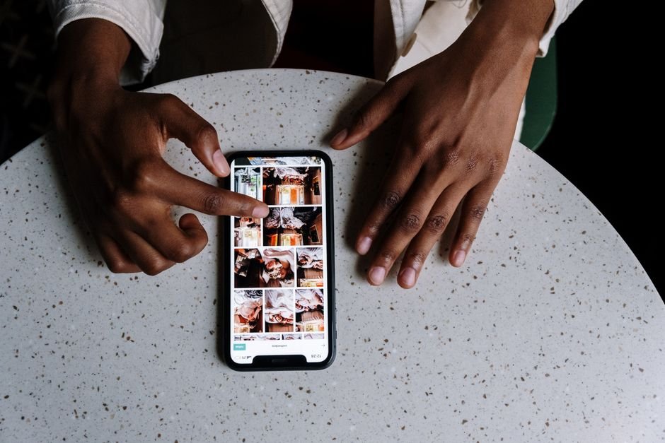 Hands interacting with smartphone displaying social media content on table in cafe setting.