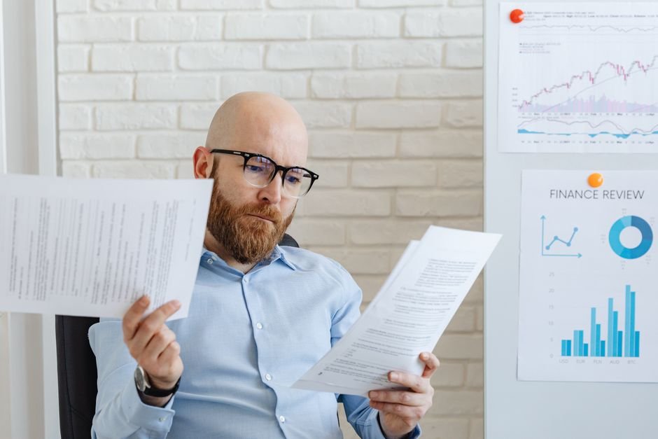 Bald bearded businessman reading financial documents in modern office setting.