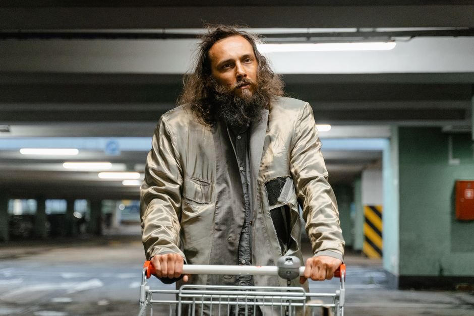 A thoughtful homeless man with a shopping cart in an urban parking structure, creating a somber mood.