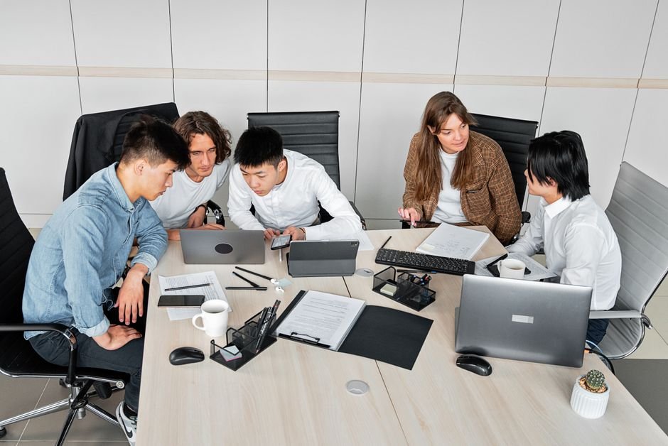 A diverse group of colleagues working together in an office setting with laptops and documents.