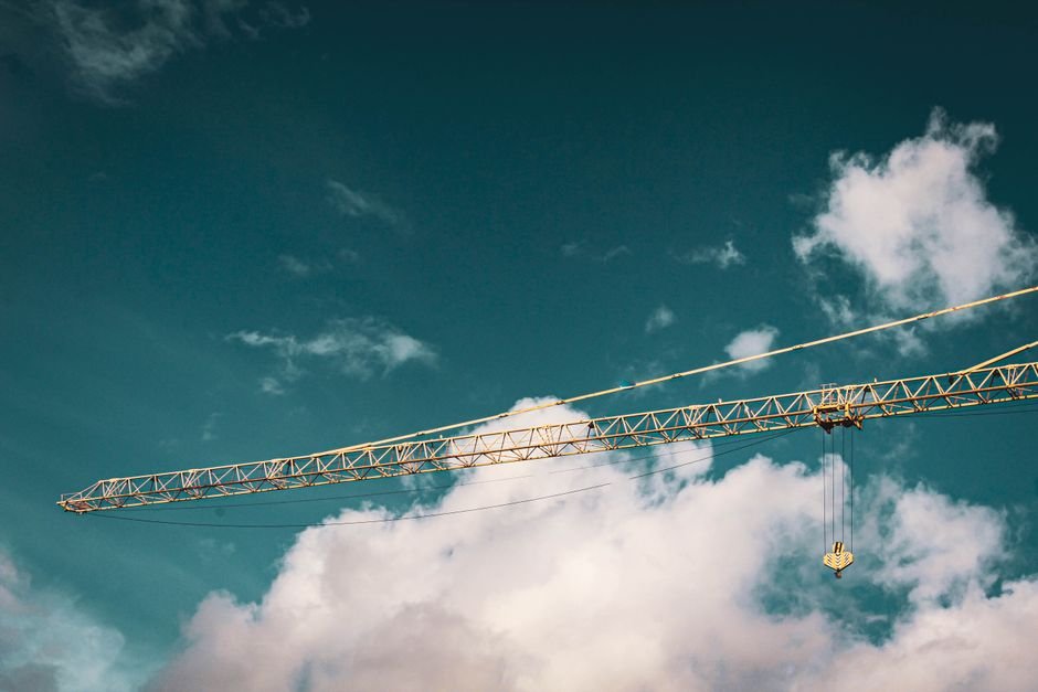 A tall tower crane set against a vibrant blue sky with fluffy clouds.