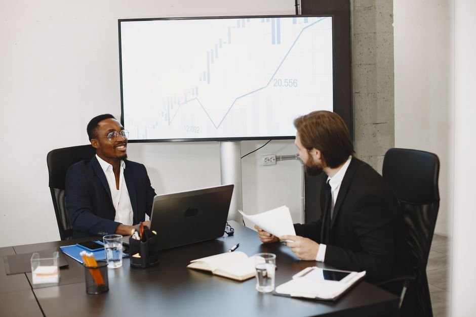 Two businessmen in a professional meeting discussing data on a large screen in a modern office.