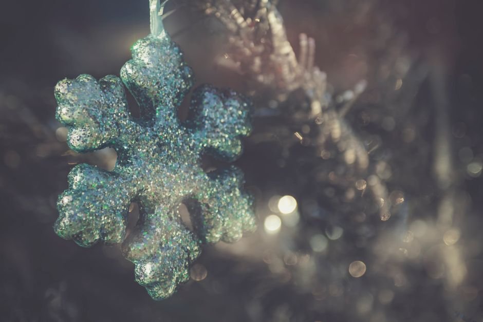 Close-up of a glittery snowflake ornament hanging on a Christmas tree branch.