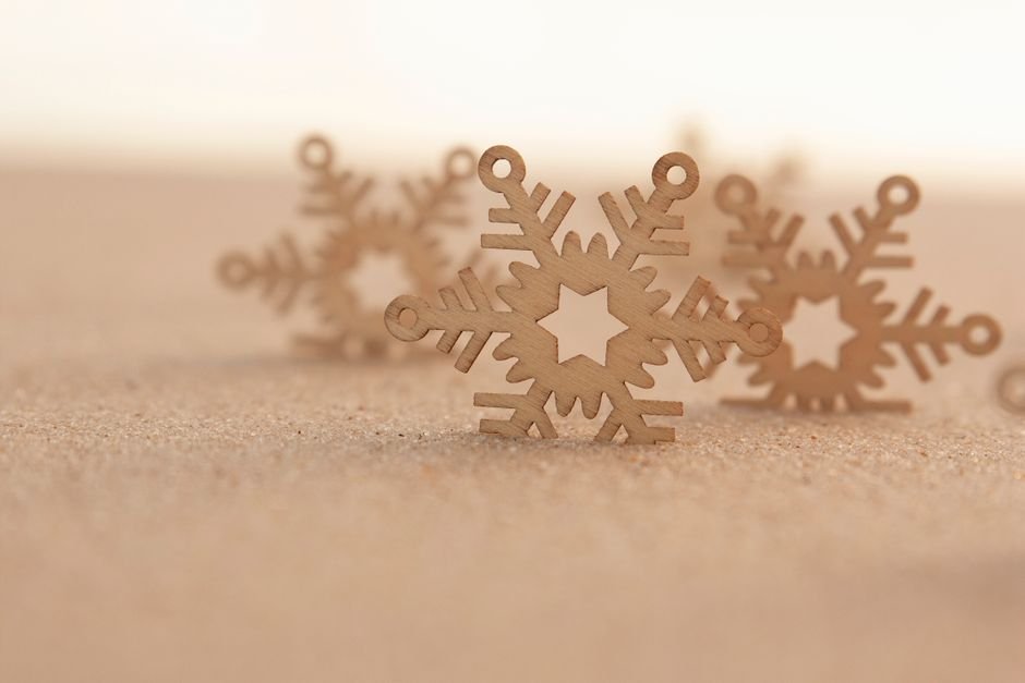 Close-up of wooden snowflake decorations on a sandy surface, evoking a simple, serene winter scene.