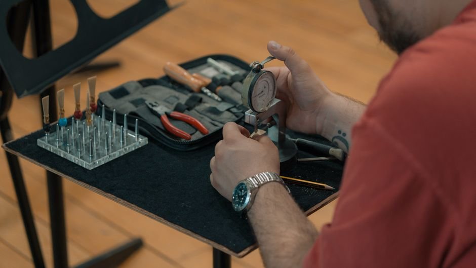 Detail shot of a musician adjusting reeds with precision tools in a workshop setting.