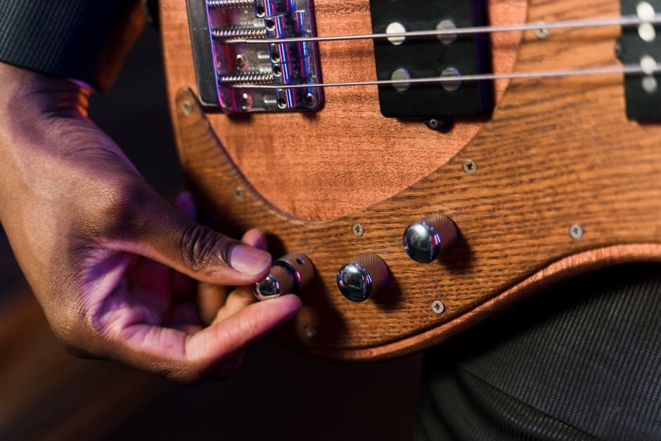 A detailed view of a hand adjusting the knob on a wooden electric guitar, showcasing intricate craftsmanship.
