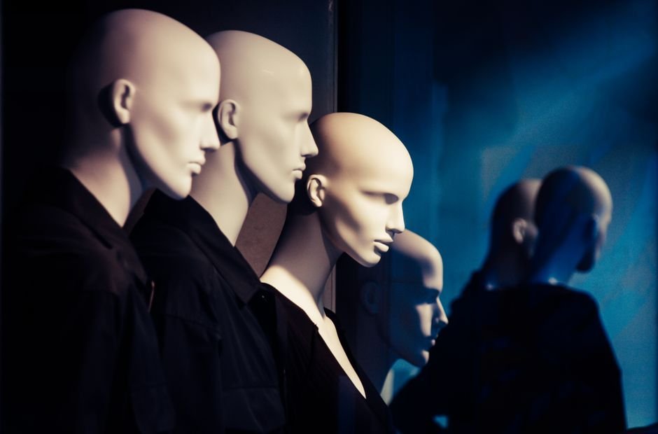 Row of mannequins in a window display with dramatic lighting creating an eerie atmosphere.
