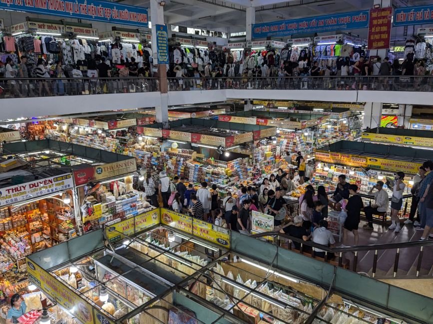 A vibrant indoor market filled with people shopping and exploring a multitude of colorful stalls and goods.