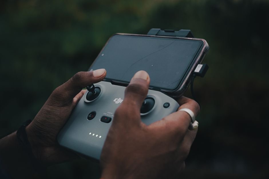 Hands holding a drone controller with smartphone attached, outdoors.