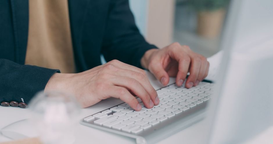 Close-up of hands typing on a white keyboard in an office setting. Ideal for business or technology themes.