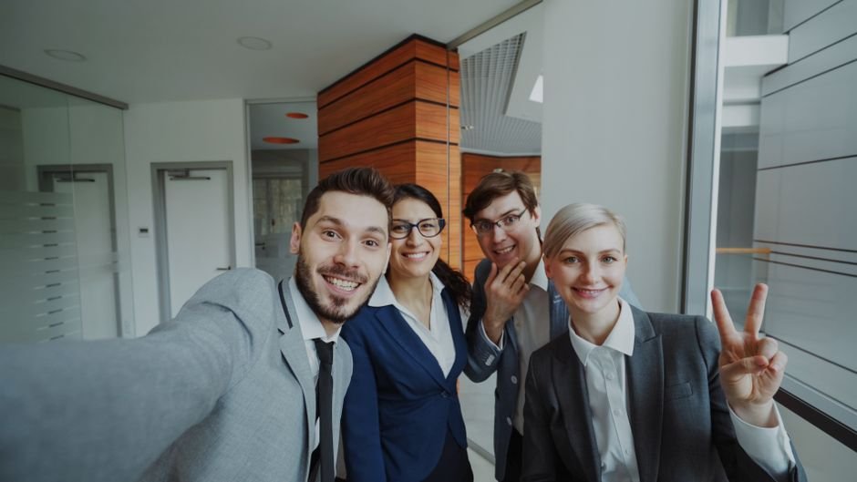 Cheerful business team posing for a group selfie in a modern office setting.