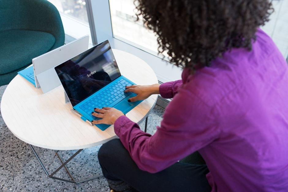 A woman typing on a laptop at a round table in a modern indoor setting.