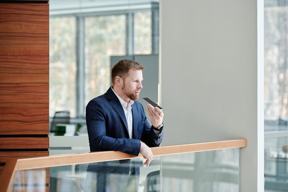 Professional businessman holding a smartphone and speaking indoors at a modern office setting.